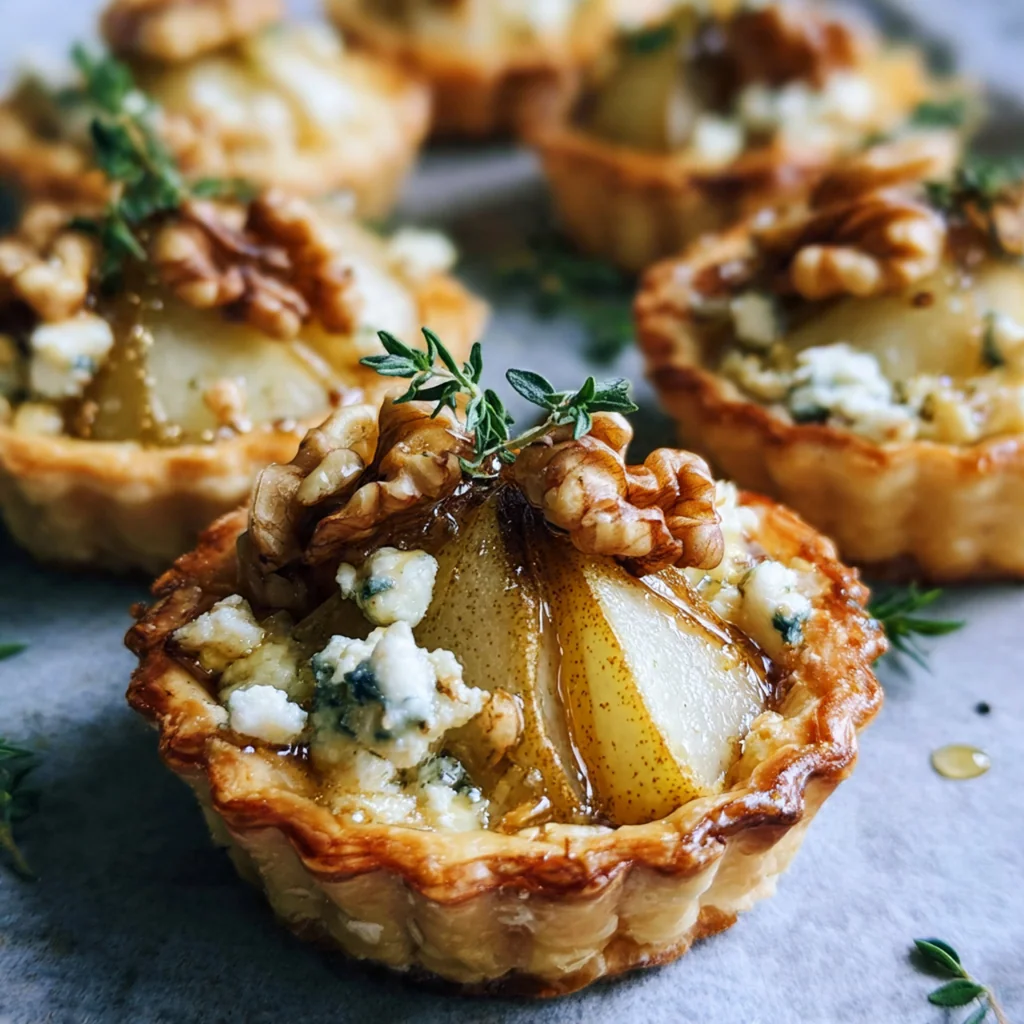 Close-up on a tartlet showing thinly sliced pears, crumbled blue cheese, and chopped walnuts